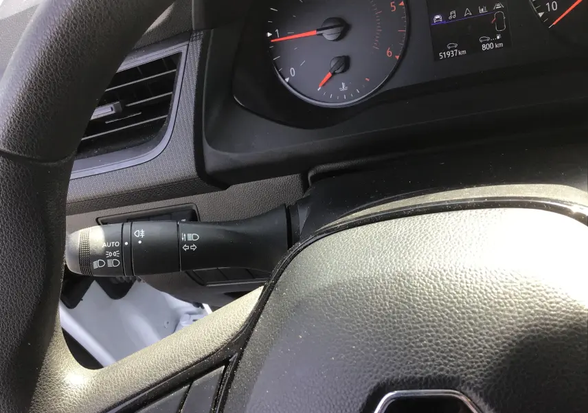 Gros plan sur le volant noir et le commodo gauche du tableau de bord du Renault Kangoo blanc 2024, avec compteurs visibles.