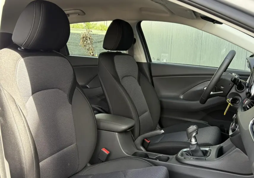 Vue intérieure côté gauche montrant les sièges avant gris foncé et l'accoudoir coulissant de la Hyundai i30 SW 2025.