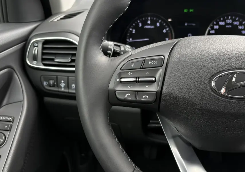 Gros plan sur le volant cuir gris foncé de la Hyundai i30 2025 avec commandes audio intégrées et tableau de bord numérique.