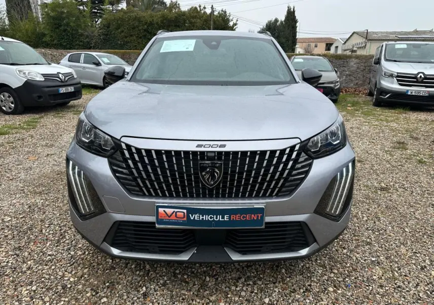 Vue avant d'un Peugeot 2008 gris 2025 avec calandre distinctive et feux LED verticaux allumés.