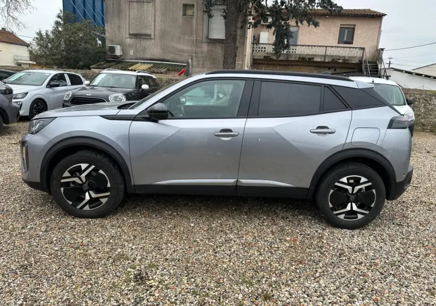 Vue de profil côté gauche d’un Peugeot 2008 Hybrid gris avec barres de toit et jantes alliage 17 pouces.