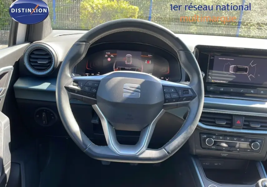 Vue intérieure centrée sur le volant cuir et le tableau de bord numérique du SEAT Arona 2025, ambiance noire moderne.