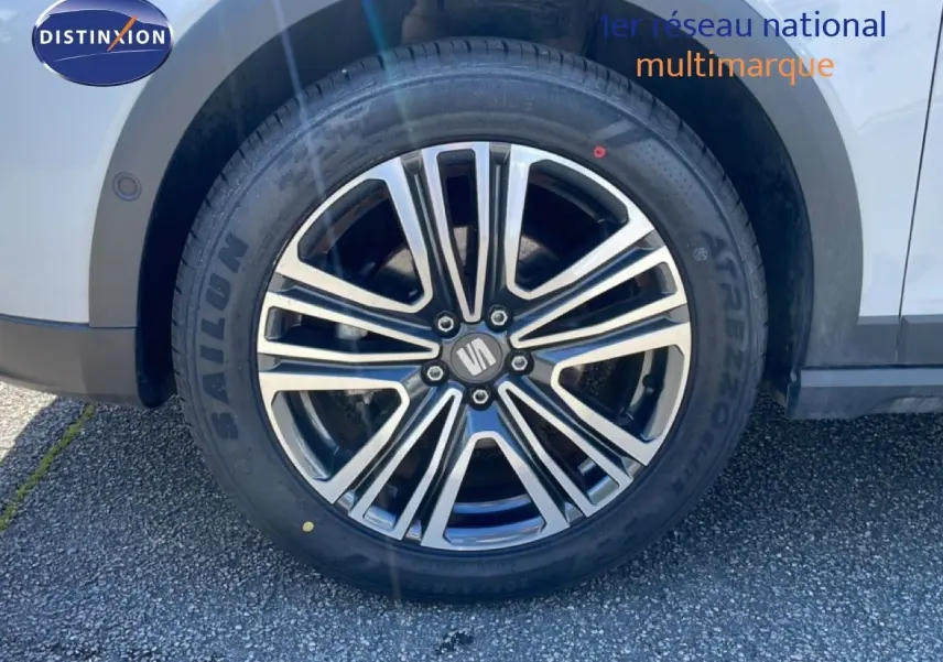 Gros plan sur la roue avant droite d’un SEAT Arona blanc avec jante alliage noire et argentée, partie de la carrosserie visible.