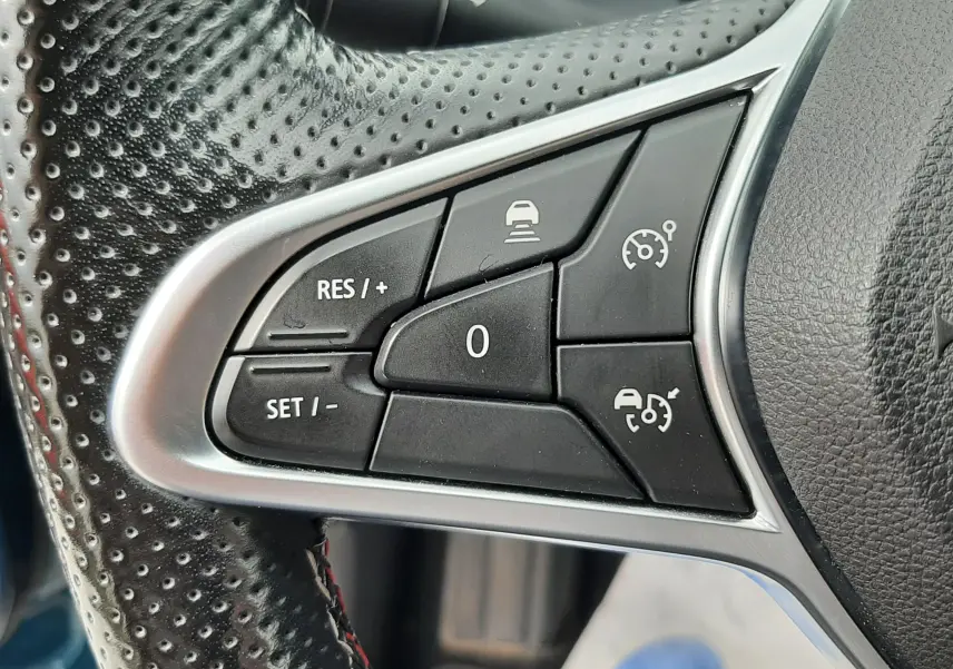 Gros plan sur les commandes noires du régulateur de vitesse au volant perforé de la Renault Arkana E-Tech.