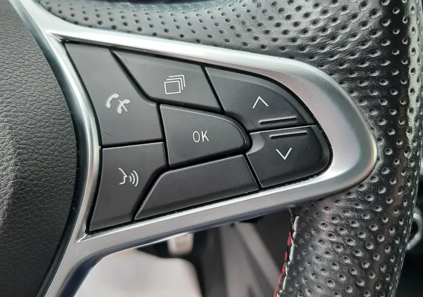 Gros plan sur les commandes noires et argentées au volant perforé d'une Renault Arkana E-Tech 145ch RS-Line.