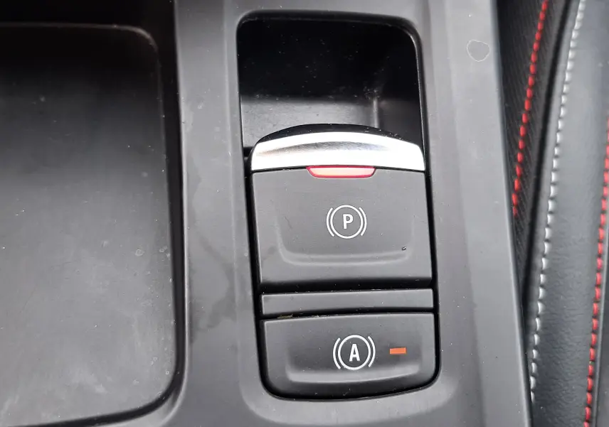 Gros plan sur les commandes de frein à main électronique et d'assistance au démarrage sur console noire avec surpiqûres rouges du Renault Arkana E-Tech.