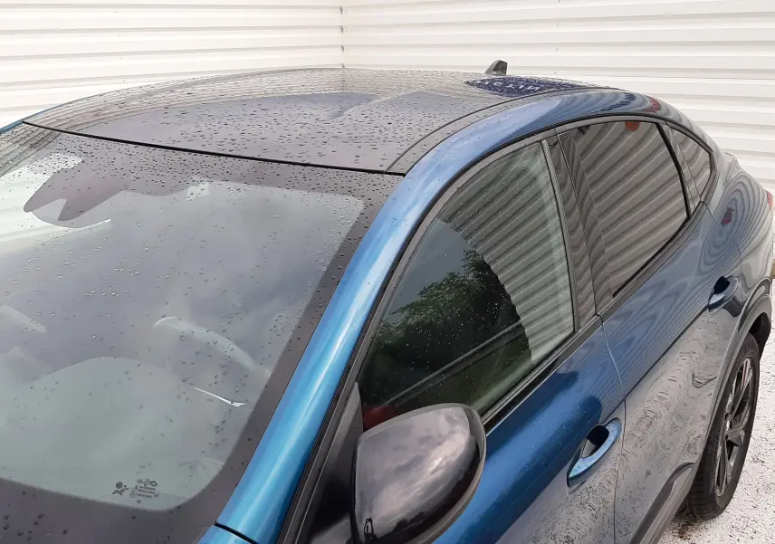 Vue 3/4 avant droit du Renault Arkana E-Tech bleu Zanzibar avec toit noir et rétroviseur noir brillant.