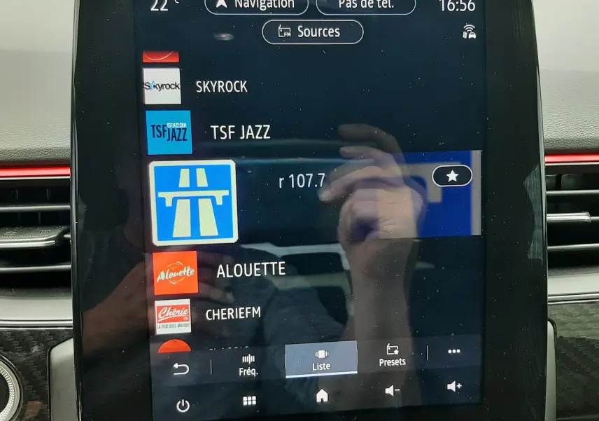 Écran tactile central du tableau de bord du Renault Arkana E-Tech bleu Zanzibar, affichant les stations radio et la navigation.