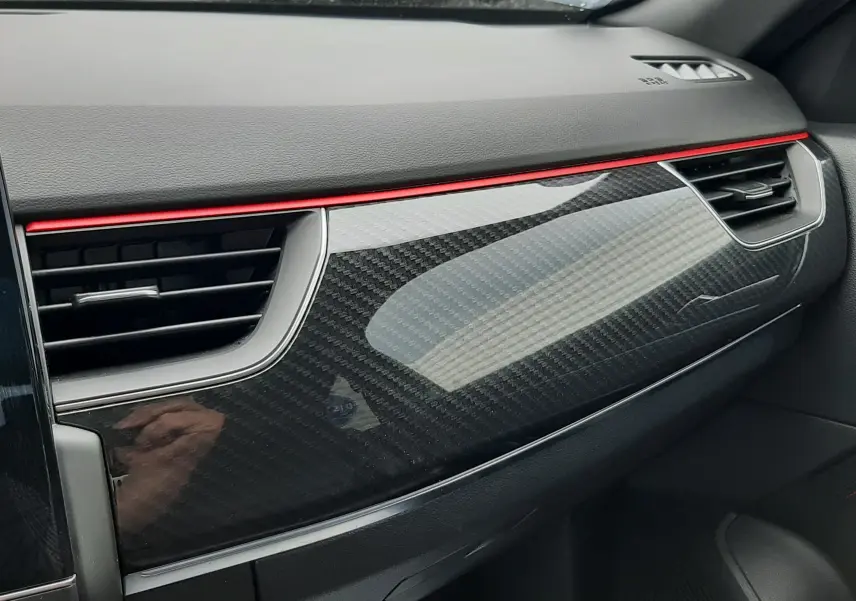 Vue intérieure côté passager du tableau de bord du Renault Arkana E-Tech 145ch RS-Line avec finition carbone et bandeau rouge.
