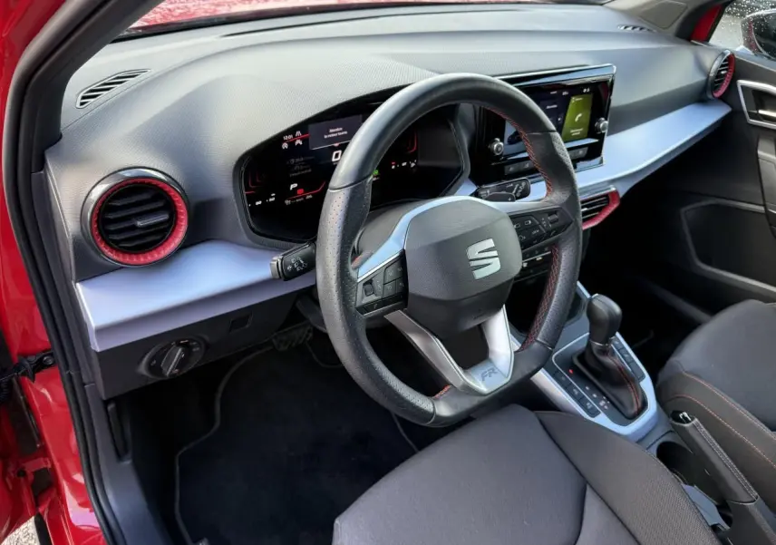 Vue intérieure côté conducteur du SEAT Arona rouge 2024, volant sport cuir Nappa avec surpiqûres rouges et tableau de bord digital.