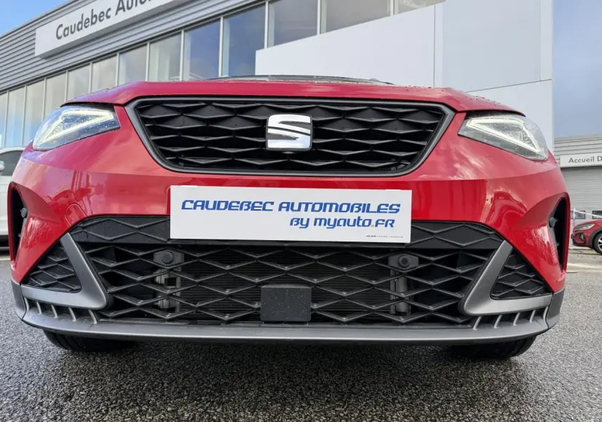 Vue avant rapprochée du SEAT Arona rouge 2024 avec calandre noire et phares Full LED allumés.