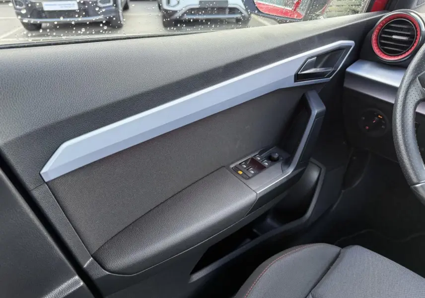 Vue intérieure côté gauche de la porte avant d'un SEAT Arona 2024 avec commandes électriques et habillage noir et gris.