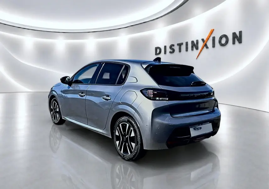 Peugeot 208 gris artense vue 3/4 arrière droit, jantes alu noires et feux arrière à LED dans un showroom lumineux.