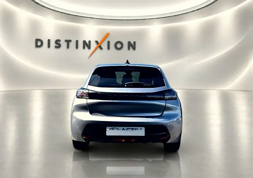 Vue arrière d'une Peugeot 208 1.2 100 Allure gris Artense dans un showroom avec éclairage doux et logo Distinxion en arrière-plan.