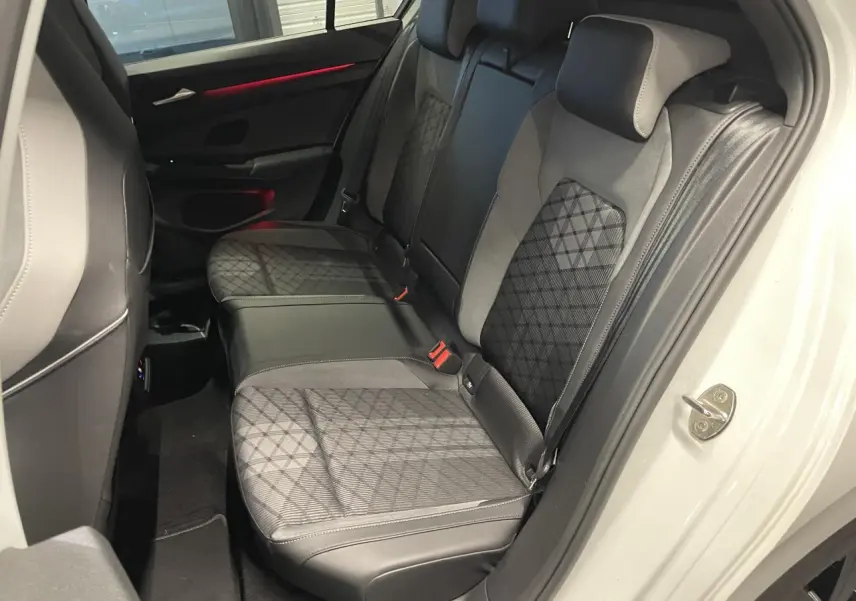 Vue intérieure de la banquette arrière en tissu noir avec motifs, porte ouverte côté droit d'une Volkswagen Golf blanche 2024.