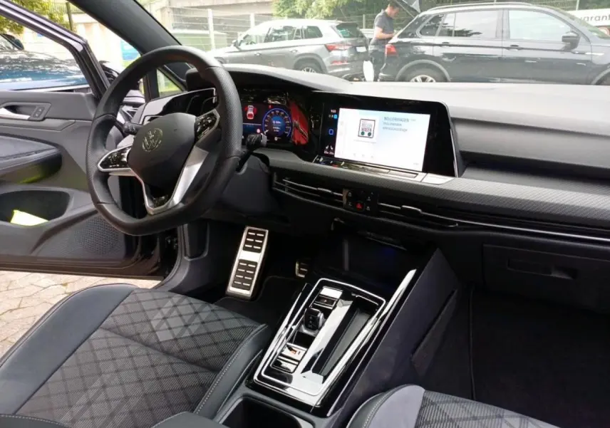 Vue intérieure côté conducteur de la Volkswagen Golf blanche 2024, avec tableau de bord digital et volant multifonctions cuir.
