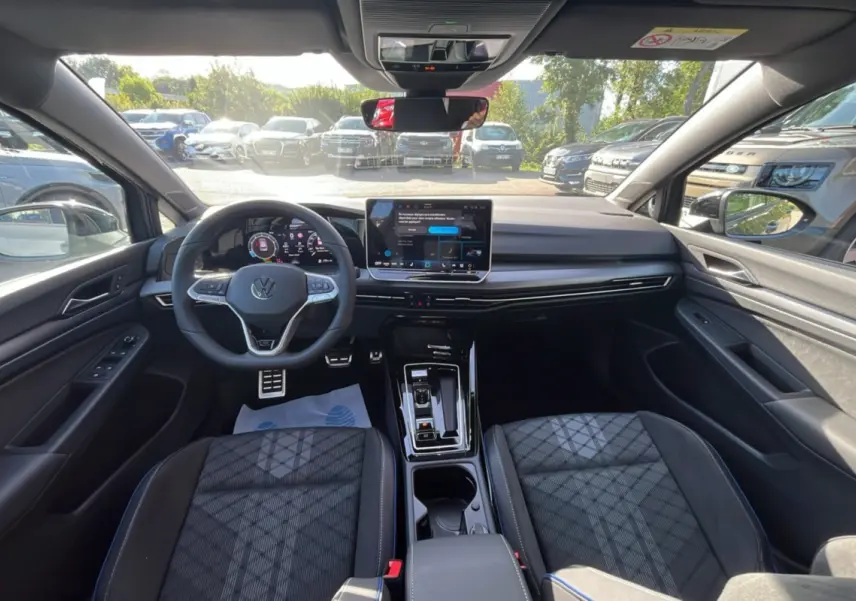 Vue intérieure avant de la Volkswagen Golf E-TSI 150 R-Line 2026, avec tableau de bord numérique et sièges tissu gris.
