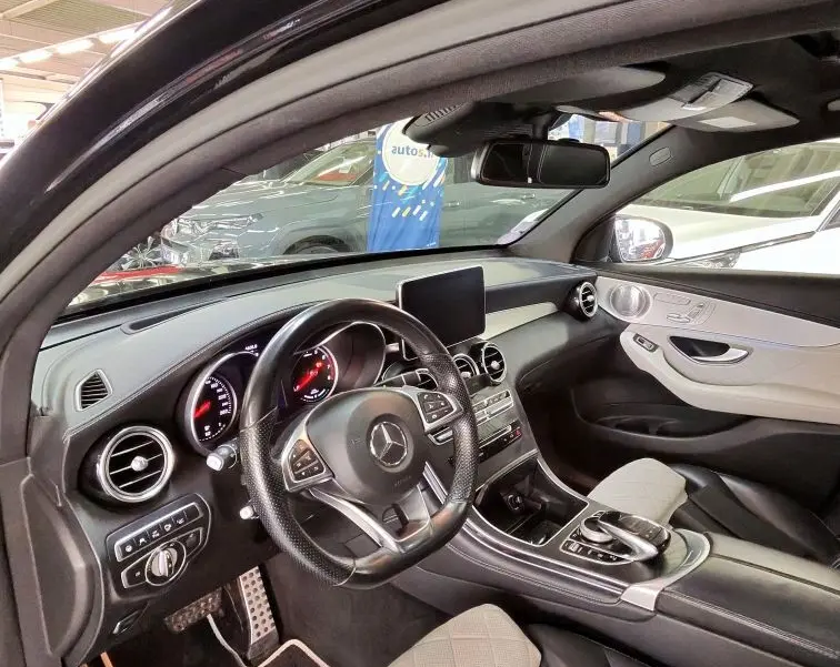 Vue intérieure côté conducteur de la Mercedes GLC 350 Coupé noire, avec sièges cuir beige et tableau de bord moderne.