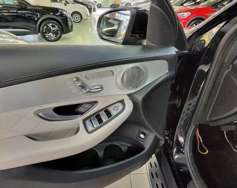 Vue intérieure côté gauche de la porte avant d’une Mercedes GLC 350 noire, mettant en valeur les commandes et la finition cuir claire.