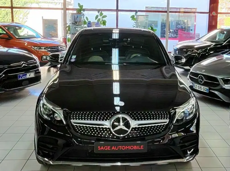 Vue frontale d'un Mercedes GLC 350 Coupé noir brillant en showroom, avec calandre diamantée et logo étoile central.