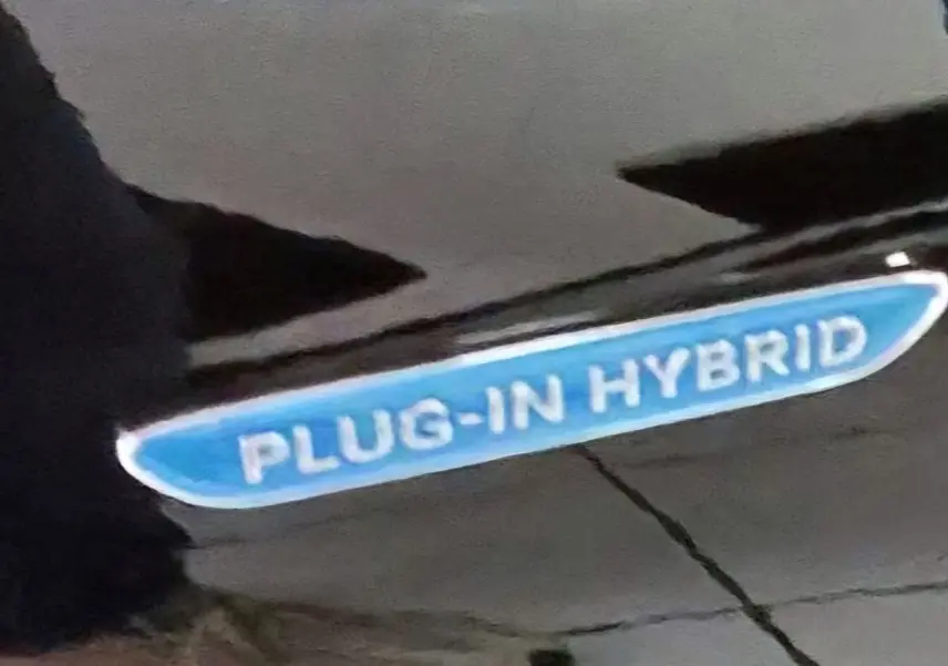 Gros plan sur l’inscription bleue "PLUG-IN HYBRID" sur la carrosserie noire d’une Mercedes GLC Coupé.