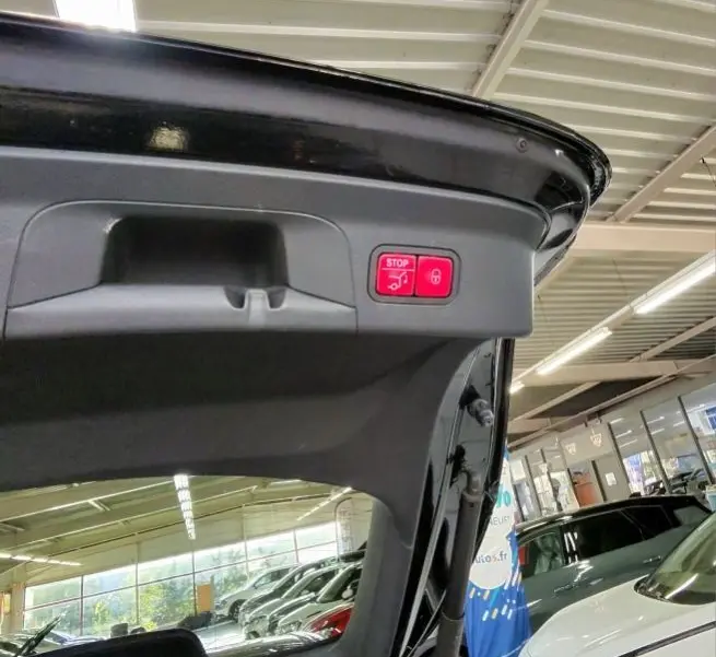 Détail intérieur du hayon ouvert d’un Mercedes GLC Coupé noir, montrant la poignée et le bouton stop électrique rouge.