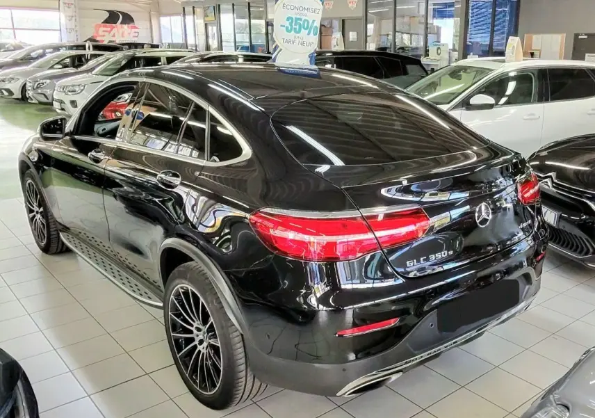 Vue 3/4 arrière droite d’un Mercedes GLC 350 Coupé noir brillant en showroom, avec feux arrière allumés et jantes noires.