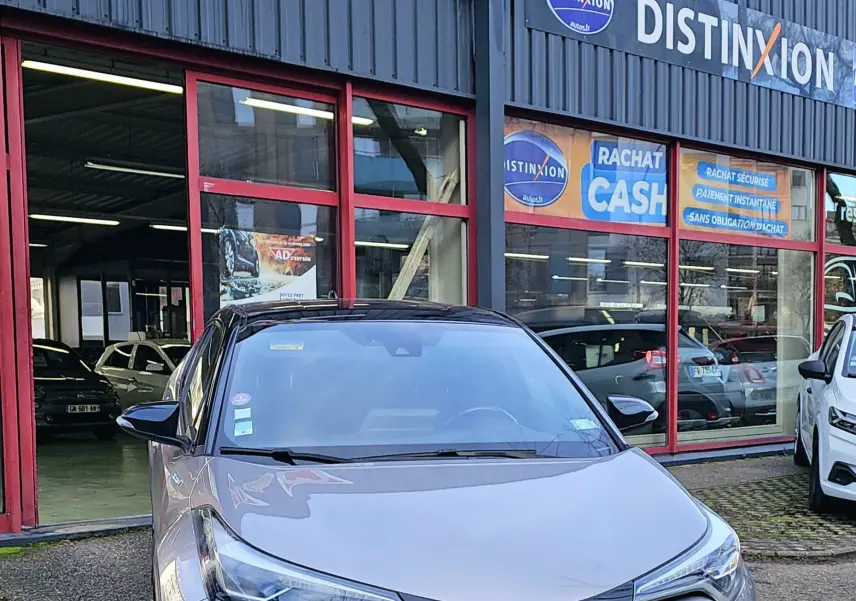 Vue avant d'un Toyota C-HR hybride gris 2018, avec calandre noire et logo bleu Toyota visible.