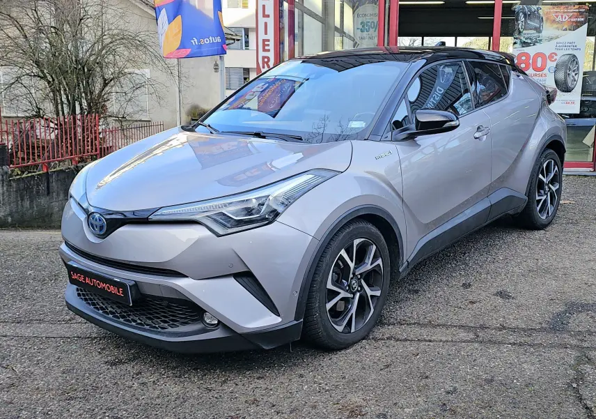 Toyota C-HR hybride gris en vue 3/4 avant droit, avec toit noir et jantes alliage distinctives.