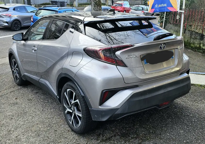 Vue 3/4 arrière droite d’un Toyota C-HR hybride gris 2018 avec toit noir et feux arrière distinctifs.