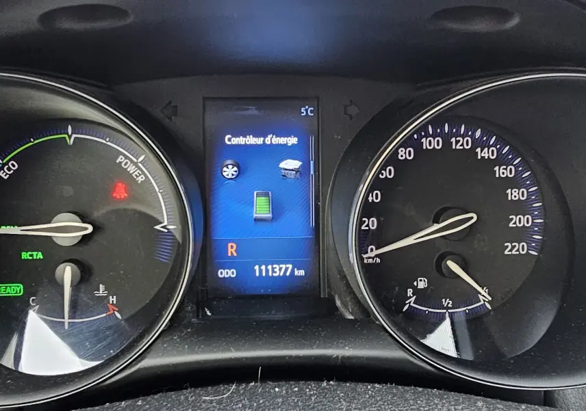 Tableau de bord du Toyota C-HR hybride gris 2018, affichage digital central et compteurs analogiques en vue frontale.