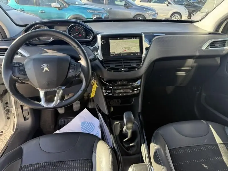 Vue intérieure de face du tableau de bord et volant noir d'une Peugeot 2008 blanche, avec écran tactile et boîte manuelle.