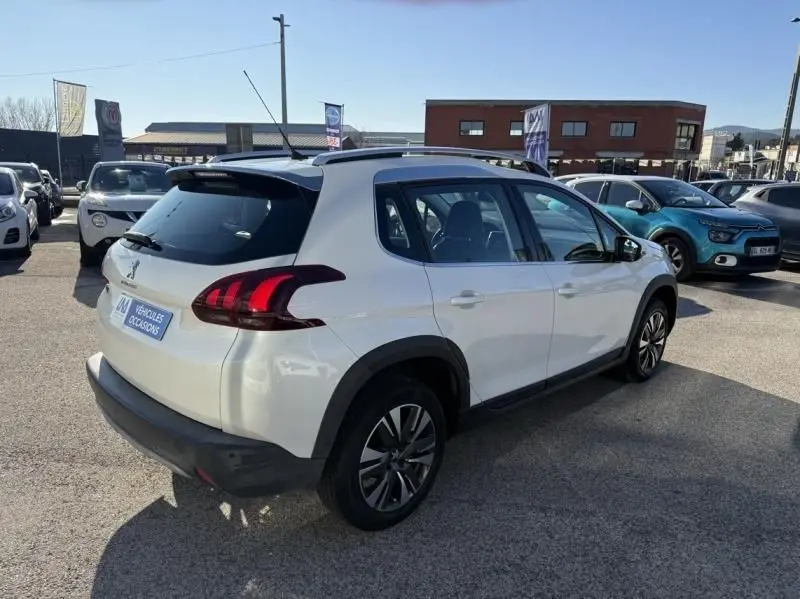 Peugeot 2008 blanc vue 3/4 arrière droit, avec feux arrière distinctifs et toit noir, en extérieur sur parking.
