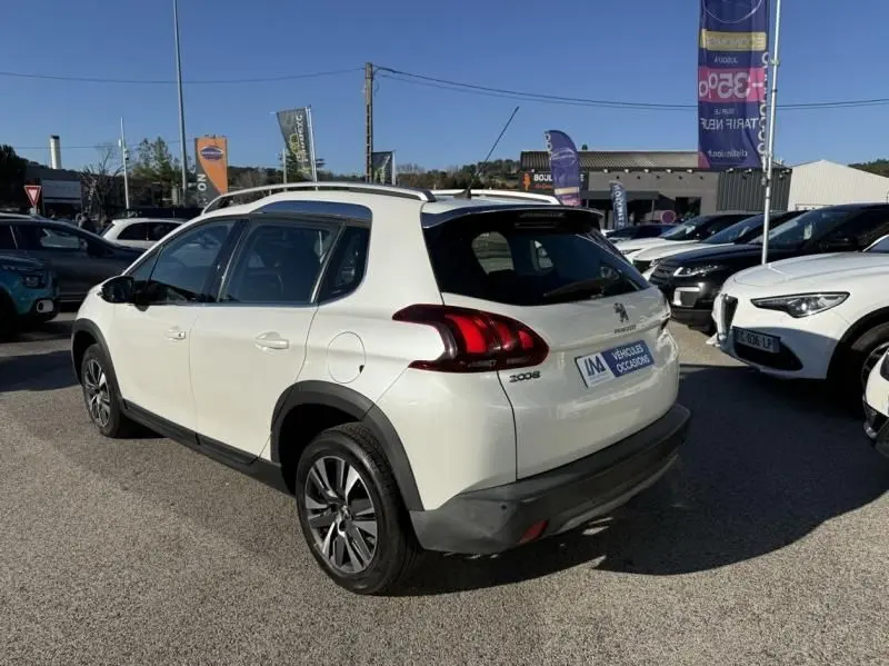 Vue 3/4 arrière droite d’un Peugeot 2008 blanc de 2018 avec feux arrière distinctifs et barres de toit visibles.