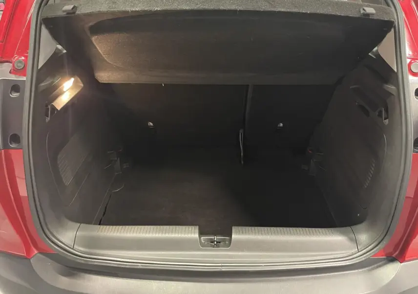 Coffre ouvert vu de l'arrière d'un Opel Crossland rouge clair, montrant l'espace de chargement vide et l'éclairage intérieur.