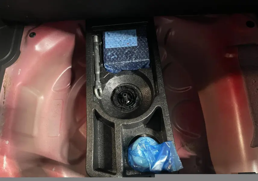 Vue rapprochée du coffre d’une Opel Crossland rouge clair montrant le rangement pour kit anti-crevaison.