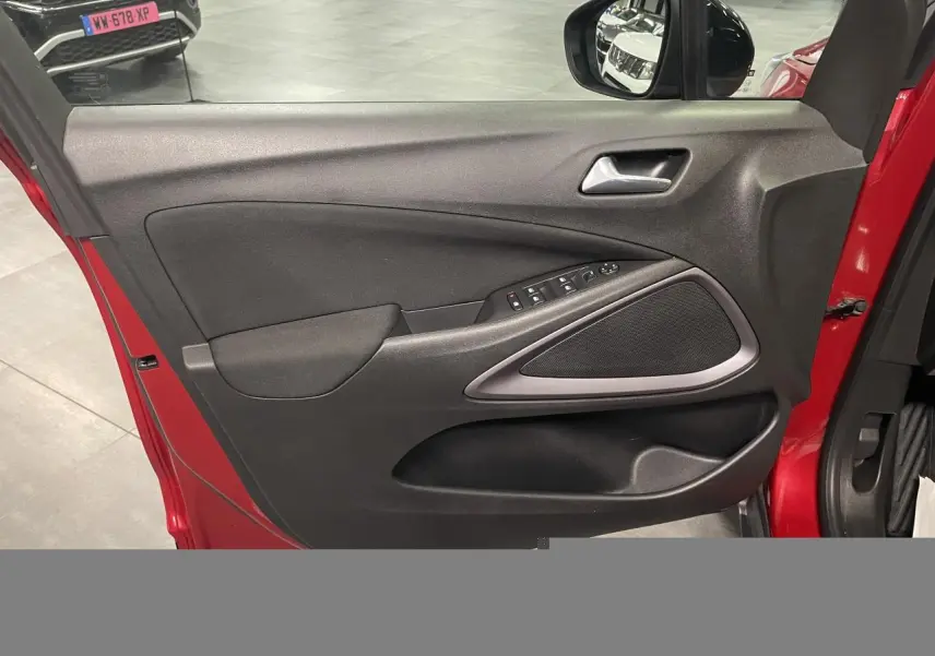 Vue intérieure de la porte avant gauche rouge clair de l’Opel Crossland avec commandes électriques et haut-parleur intégré.
