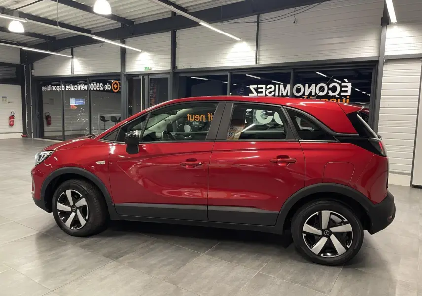 Vue latérale droite d’un Opel Crossland rouge clair 2022 avec jantes bicolores et toit assorti à la carrosserie.