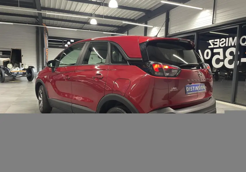 Vue 3/4 arrière droite d’un Opel Crossland rouge clair avec toit noir et jantes bicolores en intérieur showroom.