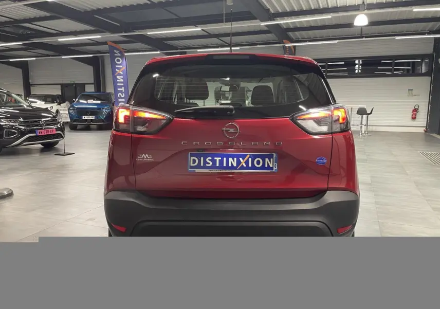 Vue arrière d'un Opel Crossland rouge clair 2022 avec feux allumés et logo Distinxion en concession.