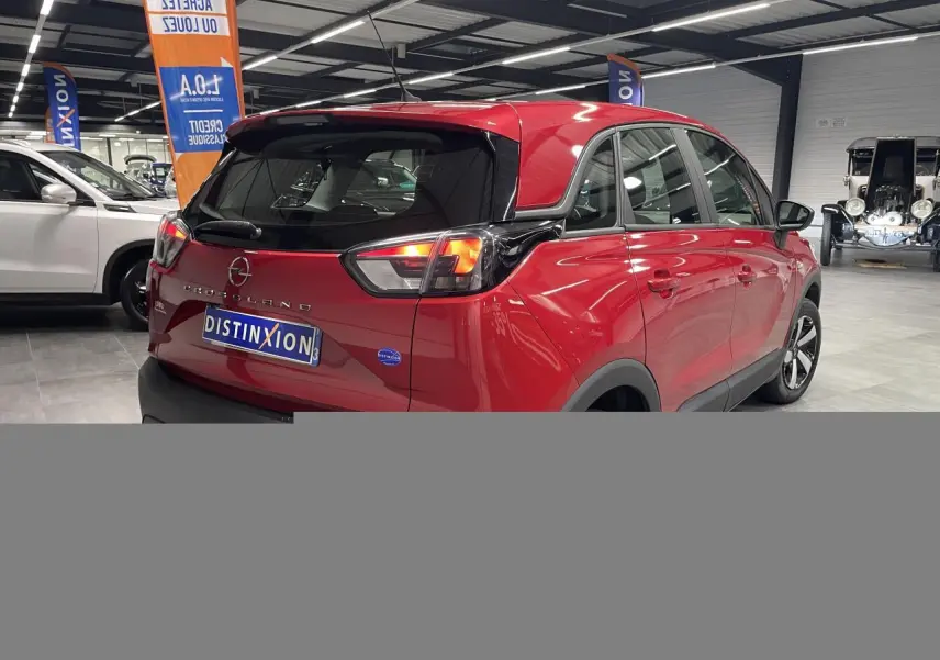 Vue 3/4 arrière droite d’un Opel Crossland rouge clair avec toit noir et jantes bicolores en showroom.