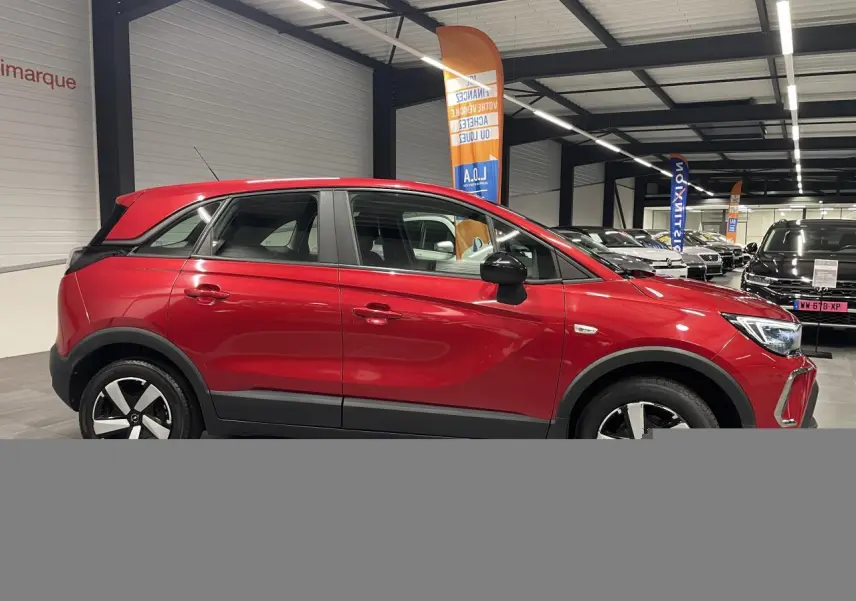Opel Crossland rouge clair vue de profil droit en intérieur, avec coques de rétroviseurs noires et jantes bicolores.