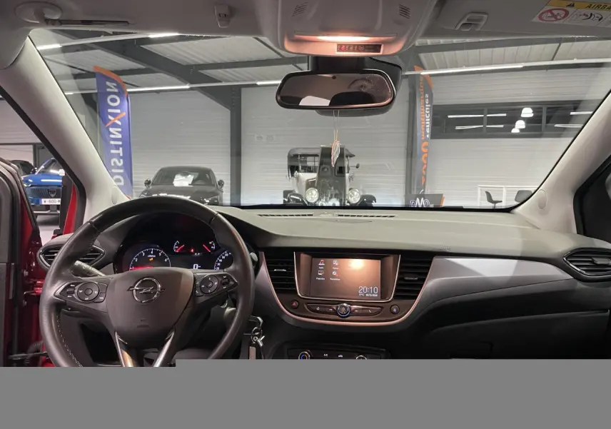 Vue intérieure avant de l'Opel Crossland rouge clair 2022, avec tableau de bord et écran tactile central allumé.