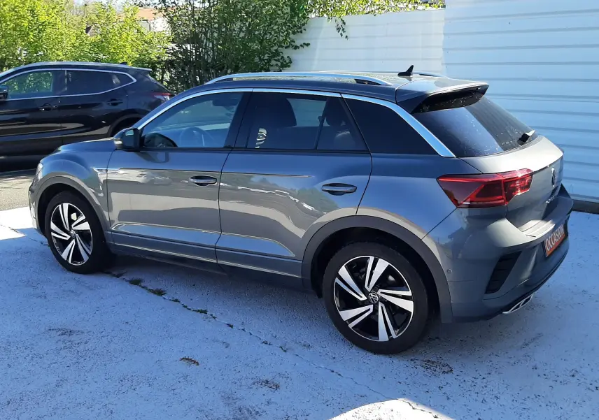 Vue 3/4 arrière droite d’un Volkswagen T-Roc gris Indium 2024 avec jantes alliage et toit noir.