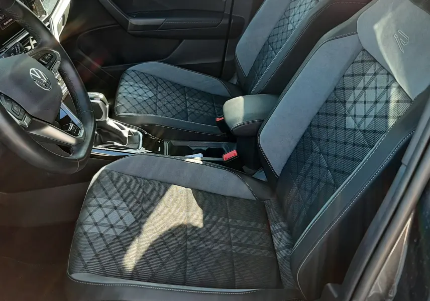 Vue intérieure côté conducteur du Volkswagen T-Roc 2024, sièges gris à motif géométrique et volant multifonction.