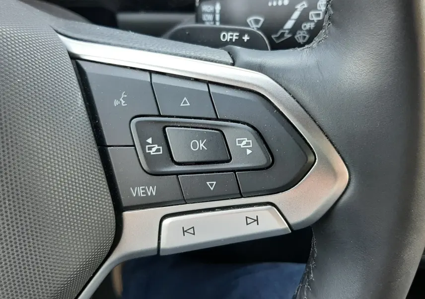 Gros plan sur les commandes multifonctions à gauche du volant noir du Volkswagen T-Roc gris Indium 2024.