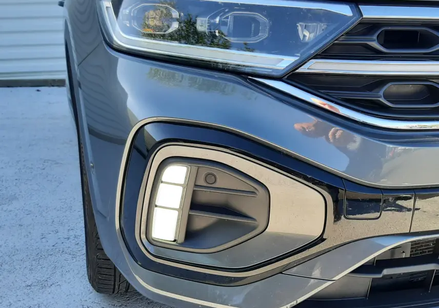 Gros plan sur l'avant gauche du Volkswagen T-Roc gris Indium, mettant en valeur le phare LED et le feu antibrouillard.