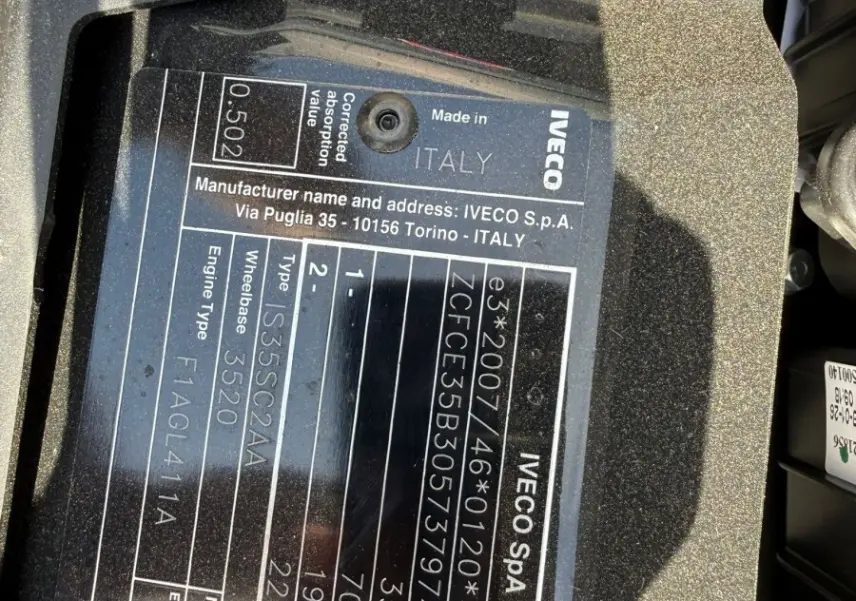 Gros plan sur la plaque constructeur noire d’un Iveco Daily blanc, montrant les détails techniques et l’origine italienne.