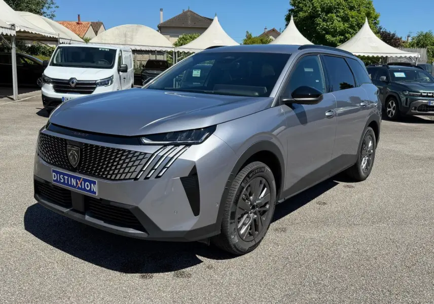 Peugeot 5008 gris clair en 3/4 avant droit, avec calandre distinctive et phares LED fins, sur parking extérieur.