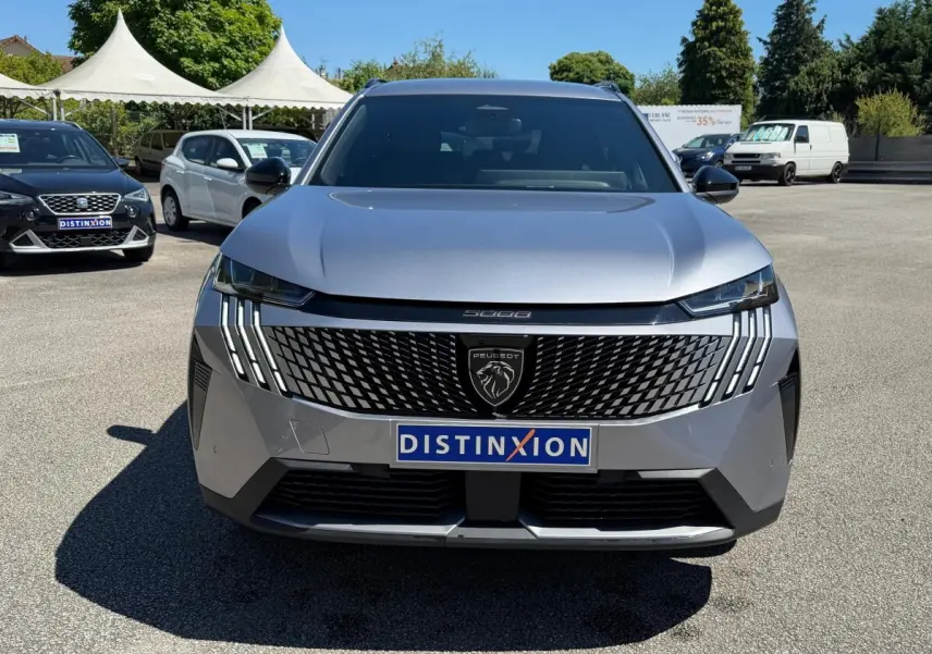 Vue de face d’un Peugeot 5008 gris clair 2025 avec calandre noire distinctive et feux LED verticaux.